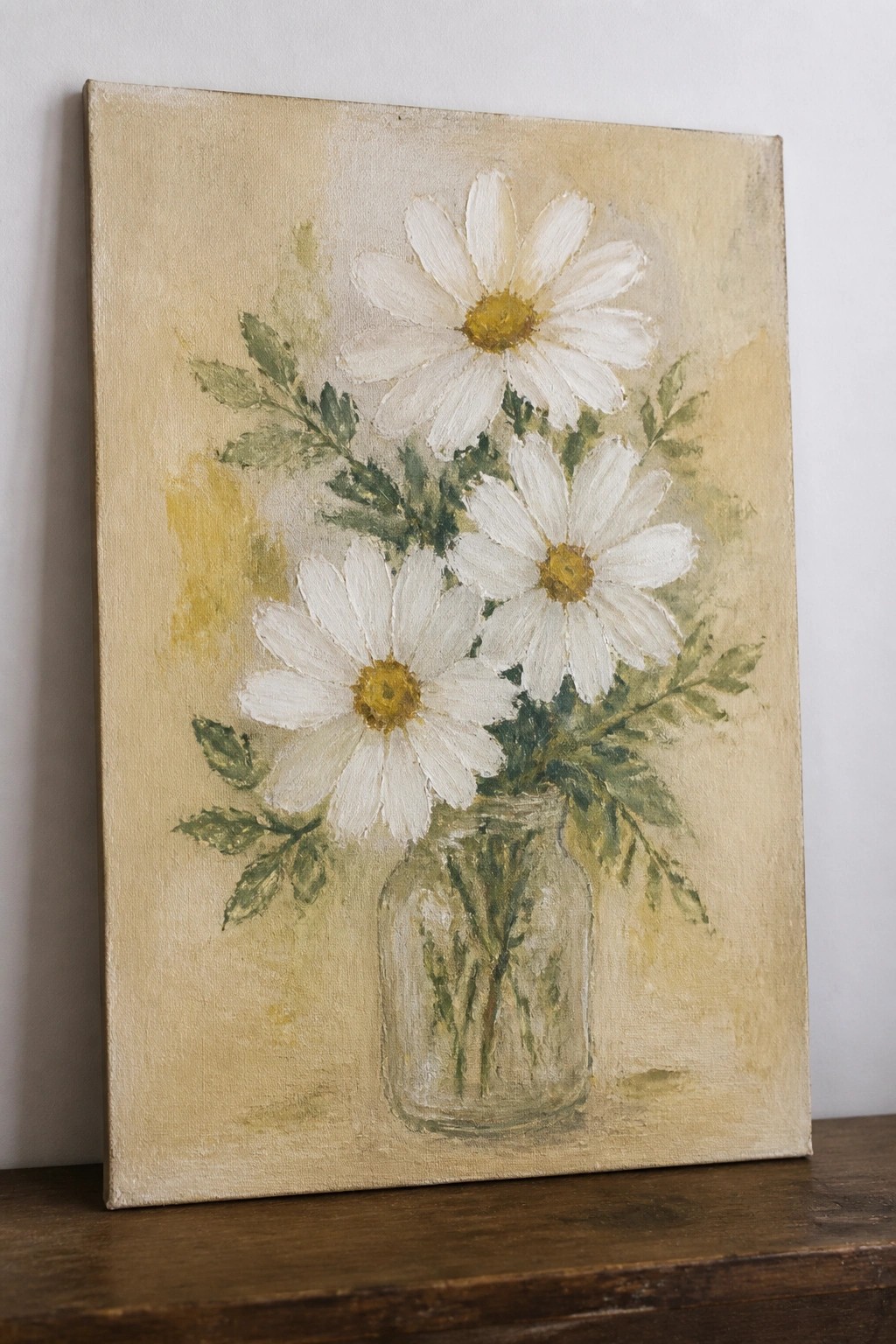Three white daisies with yellow centers in a glass jar on wood