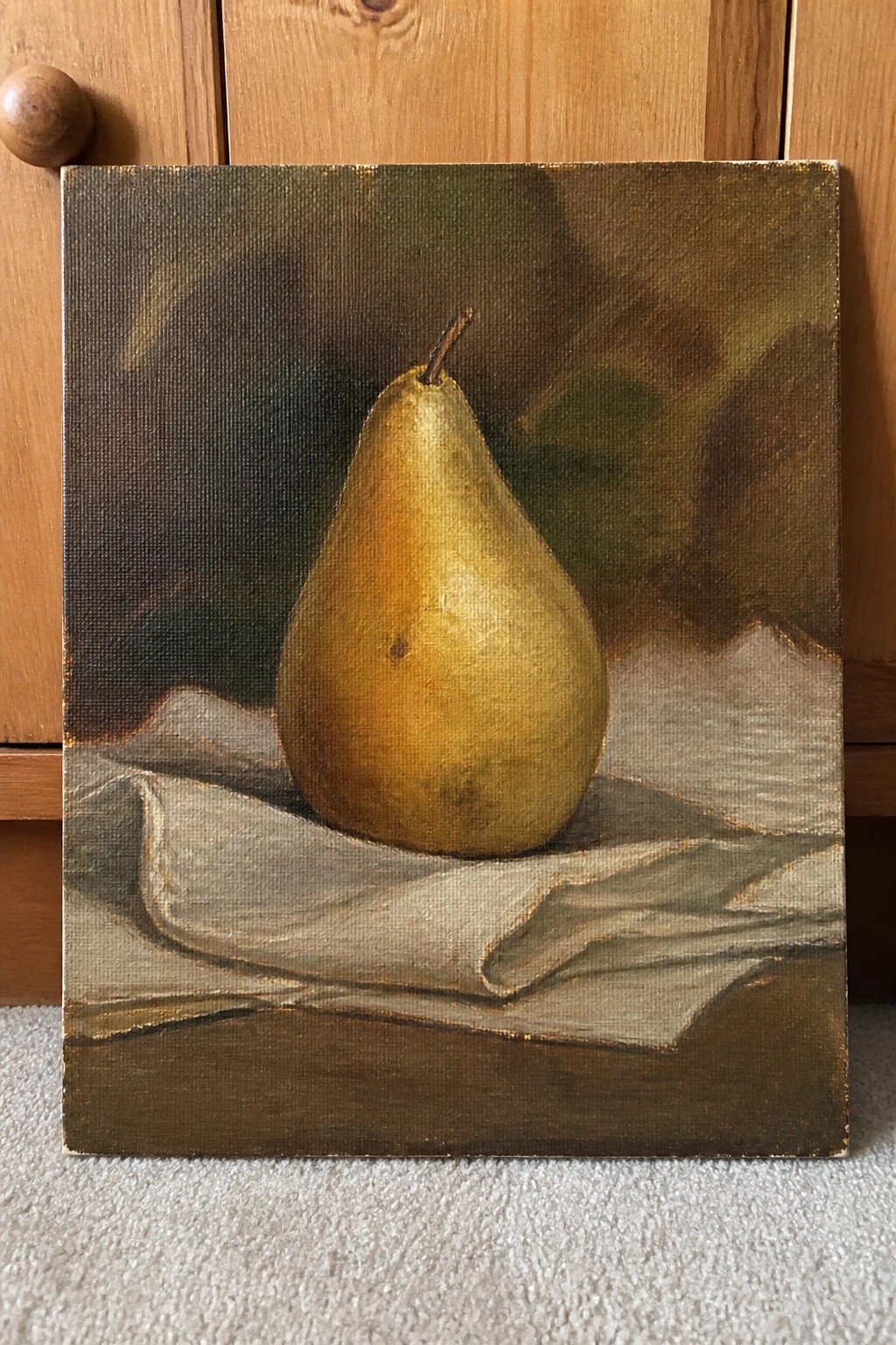 Realistic still life painting of a yellow pear on rumpled white fabric