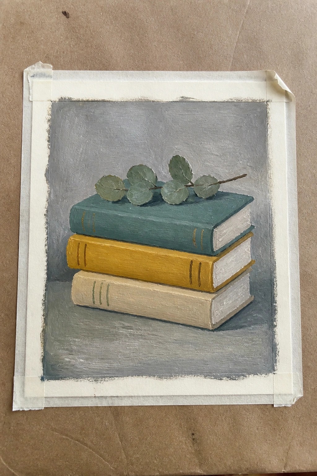 Stack of three books in teal, yellow, and beige with eucalyptus leaves on top