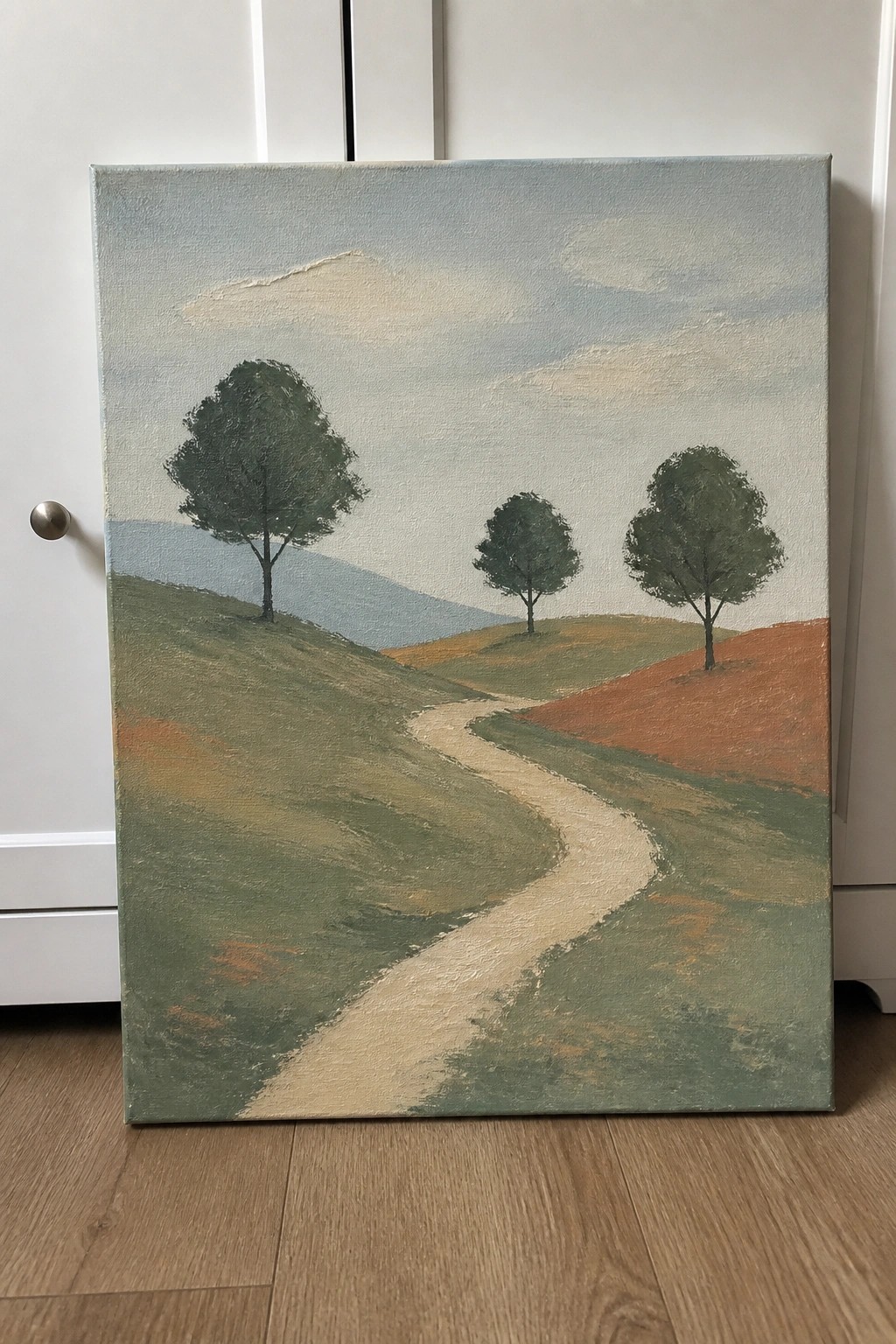 Canvas painting of winding path through green hills with three trees under cloudy sky