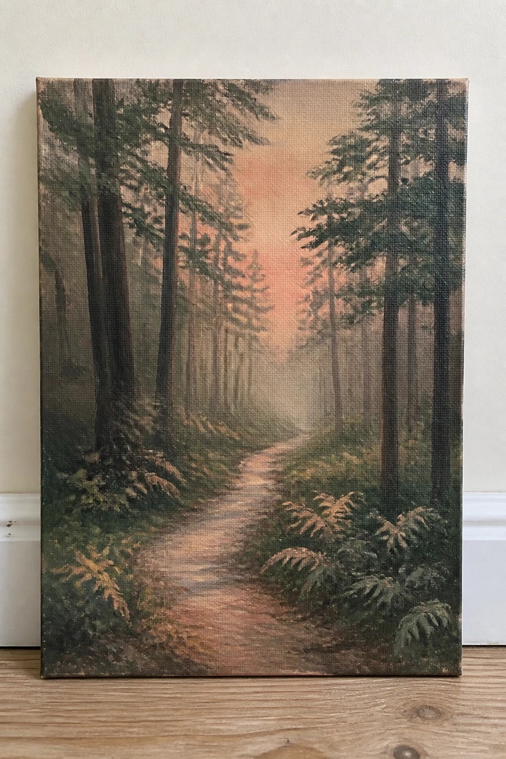 Winding dirt path through misty forest of tall trees under orange sunset sky.
