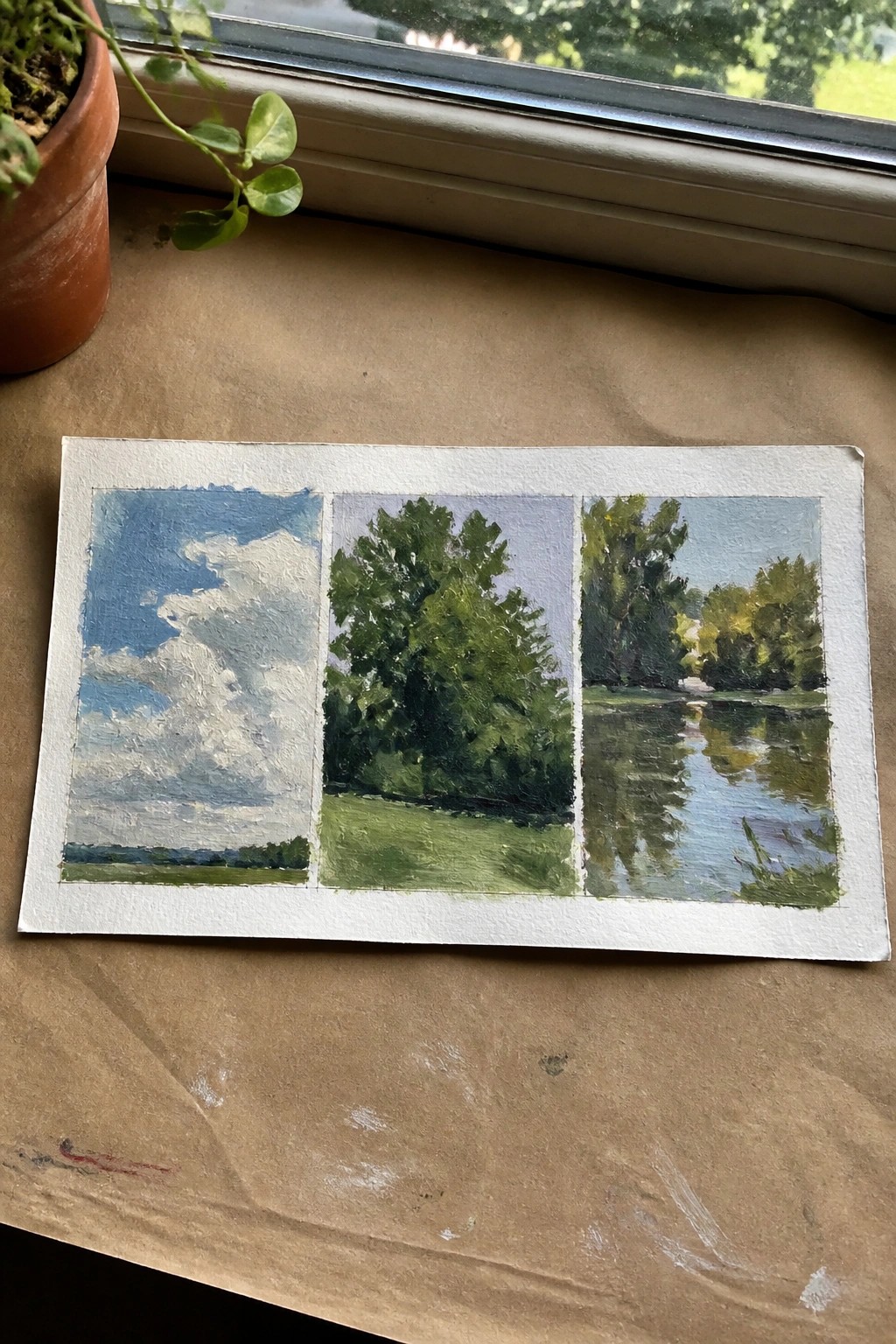 Three-panel landscape study with blue sky, green trees, and water reflections beside potted plant