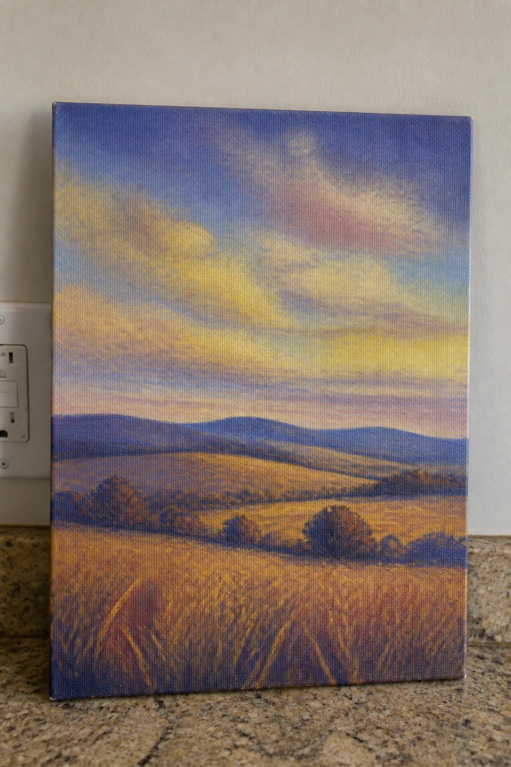 Vibrant landscape painting of golden fields, blue hills, and colorful sunset sky on canvas.