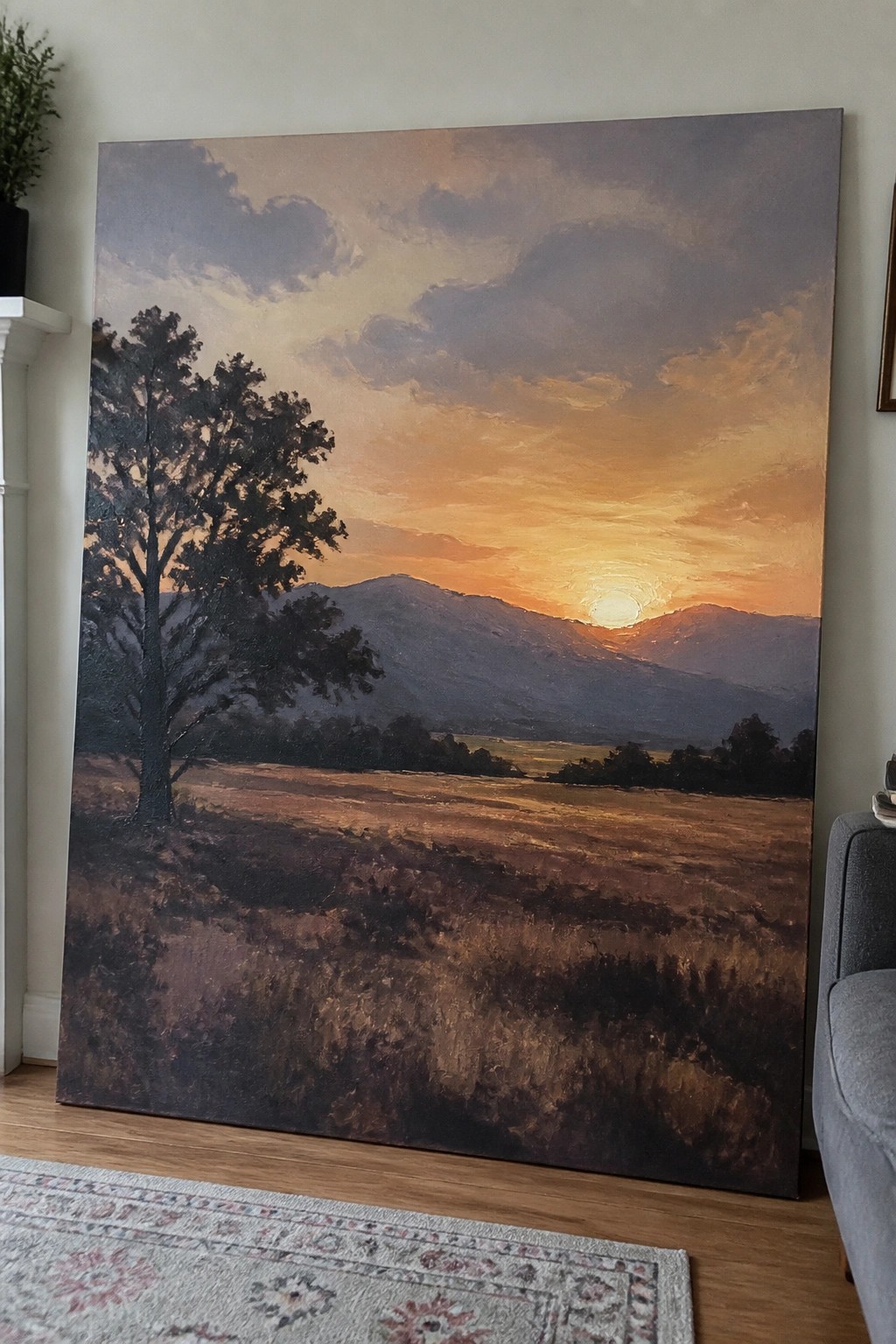 Large oil painting of sunset over mountains with lone tree in golden field