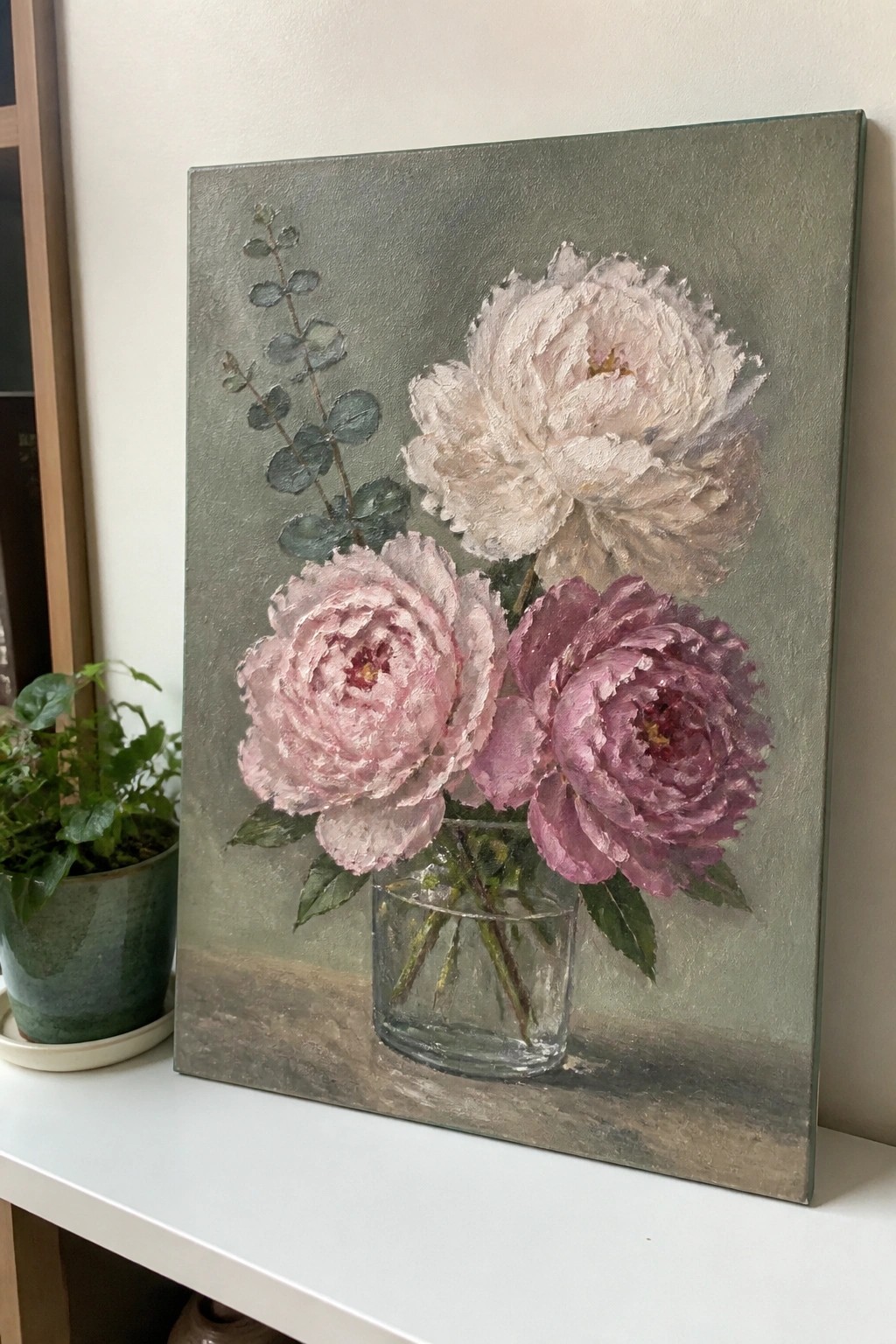 Pink and purple peonies in a glass vase against a muted green background
