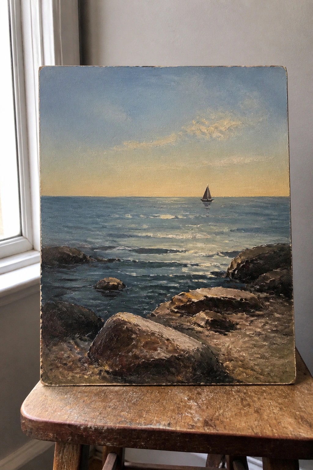 Rocky shoreline meets blue ocean waves with distant sailboat under gradient sunset sky on stool