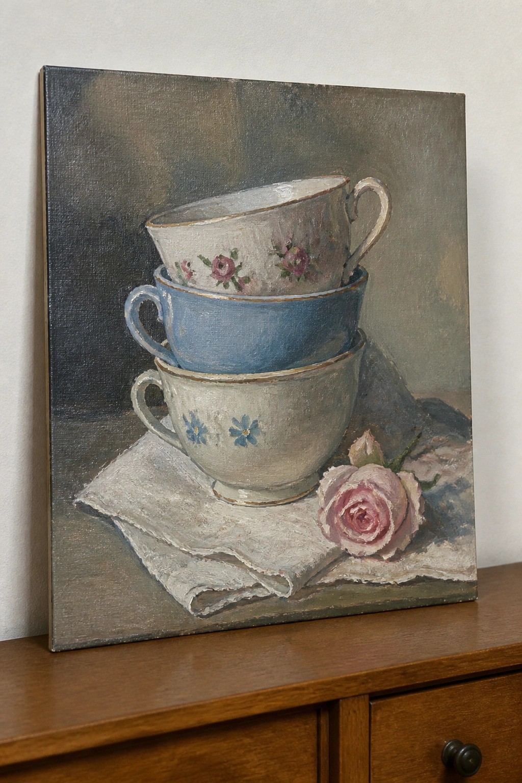 Three stacked floral teacups with pink rose on white cloth still life painting