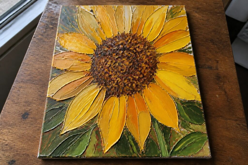 22 Palette Knife Acrylic Painting Ideas With Rich Textured Dimension Thick impasto painting of a vibrant yellow sunflower with green leaves on wood.