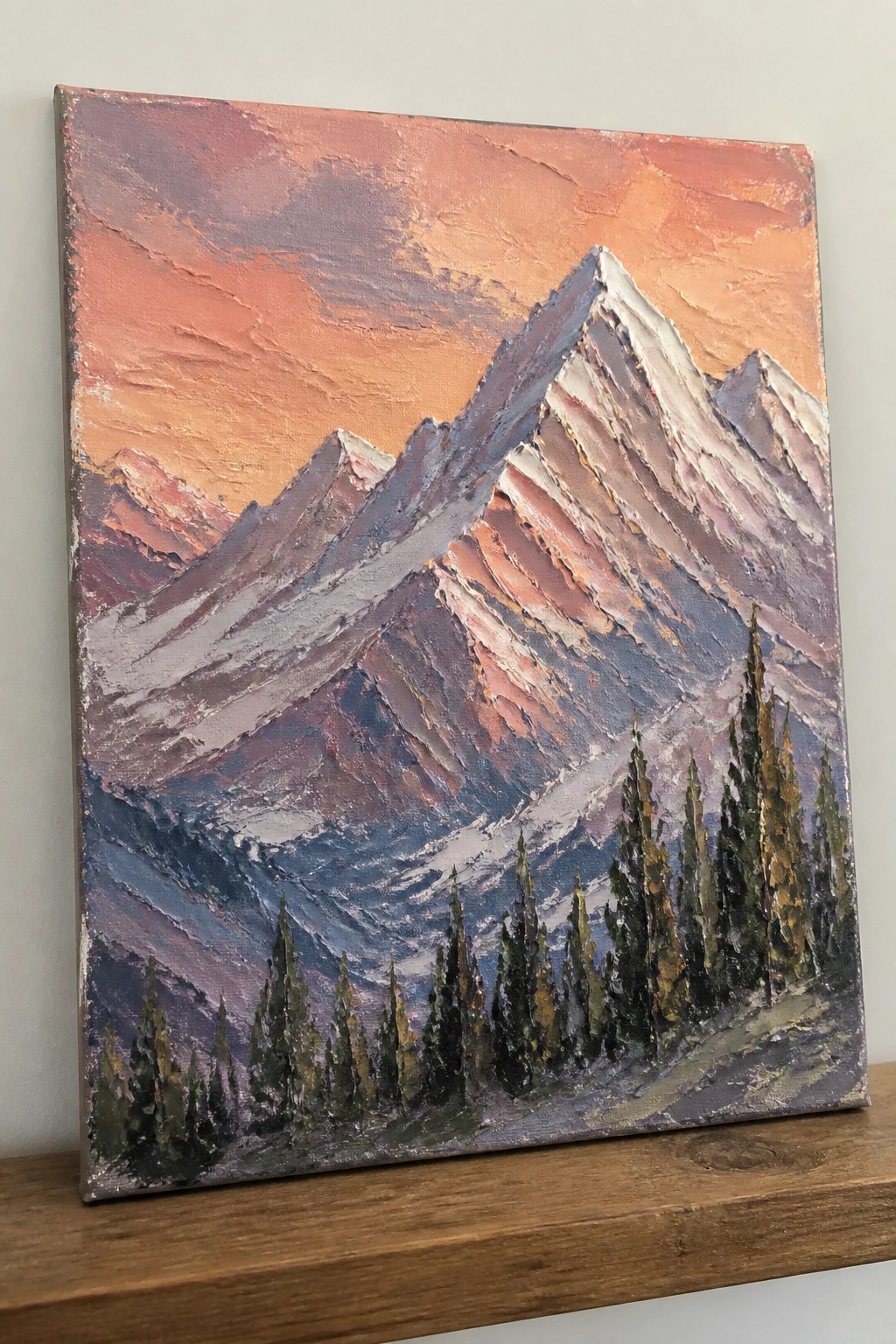 Textured painting of snow-capped mountains under vibrant orange-pink sunset sky with pine trees.