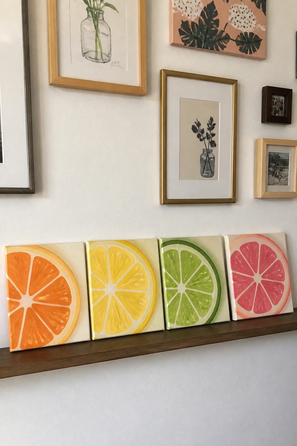 Four citrus slice paintings on canvases lined up along a wooden shelf.