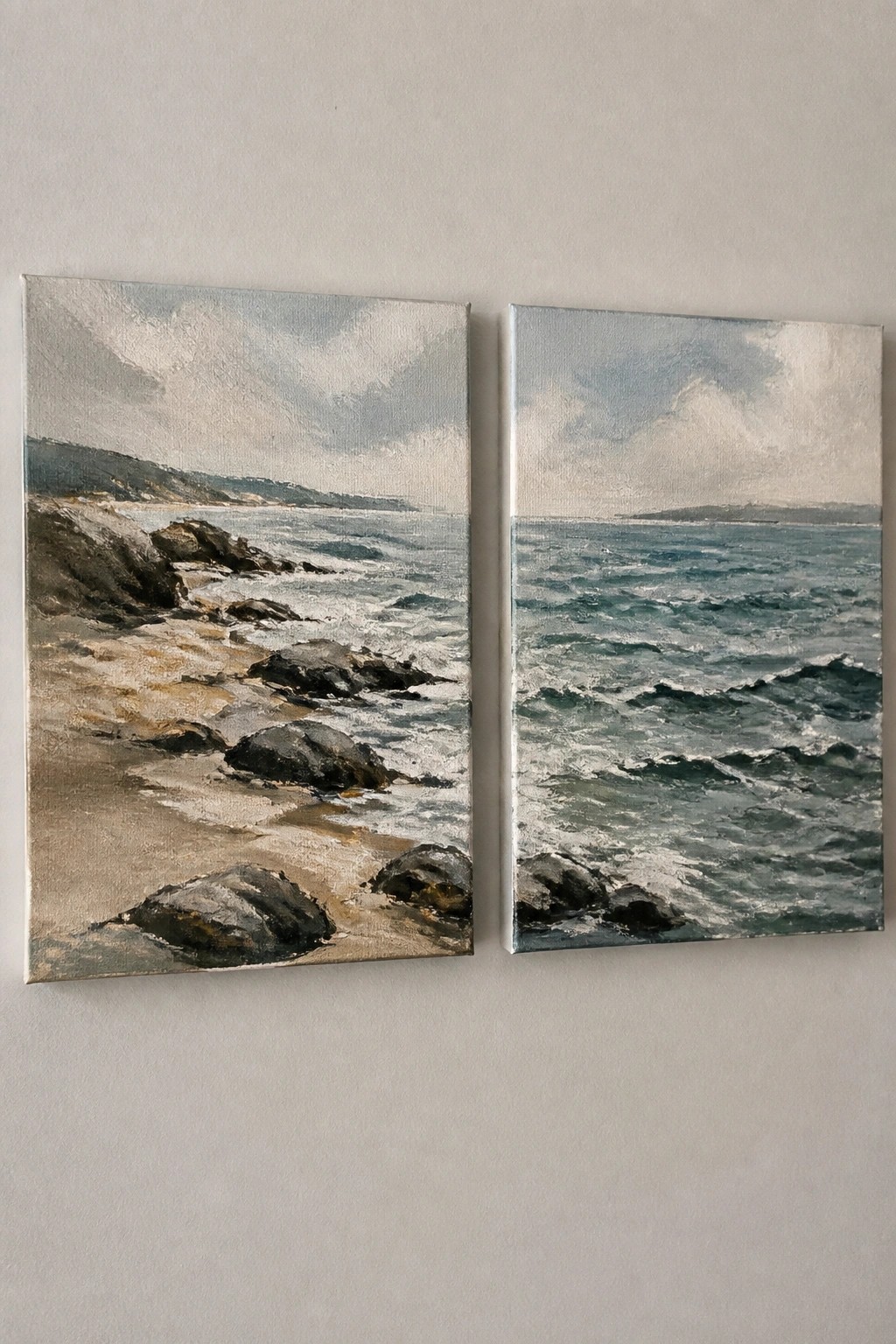 Two side-by-side seascape paintings on a wall showing rocky shores and blue ocean waves