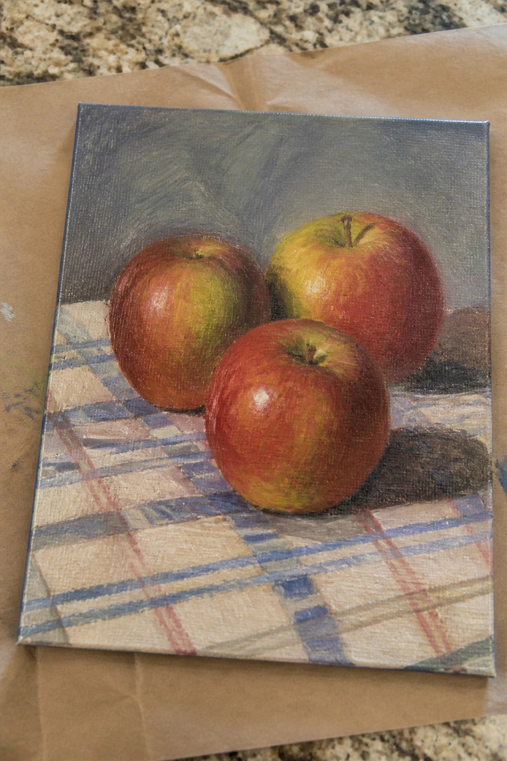 Three red and yellow apples on blue checkered cloth in oil painting.