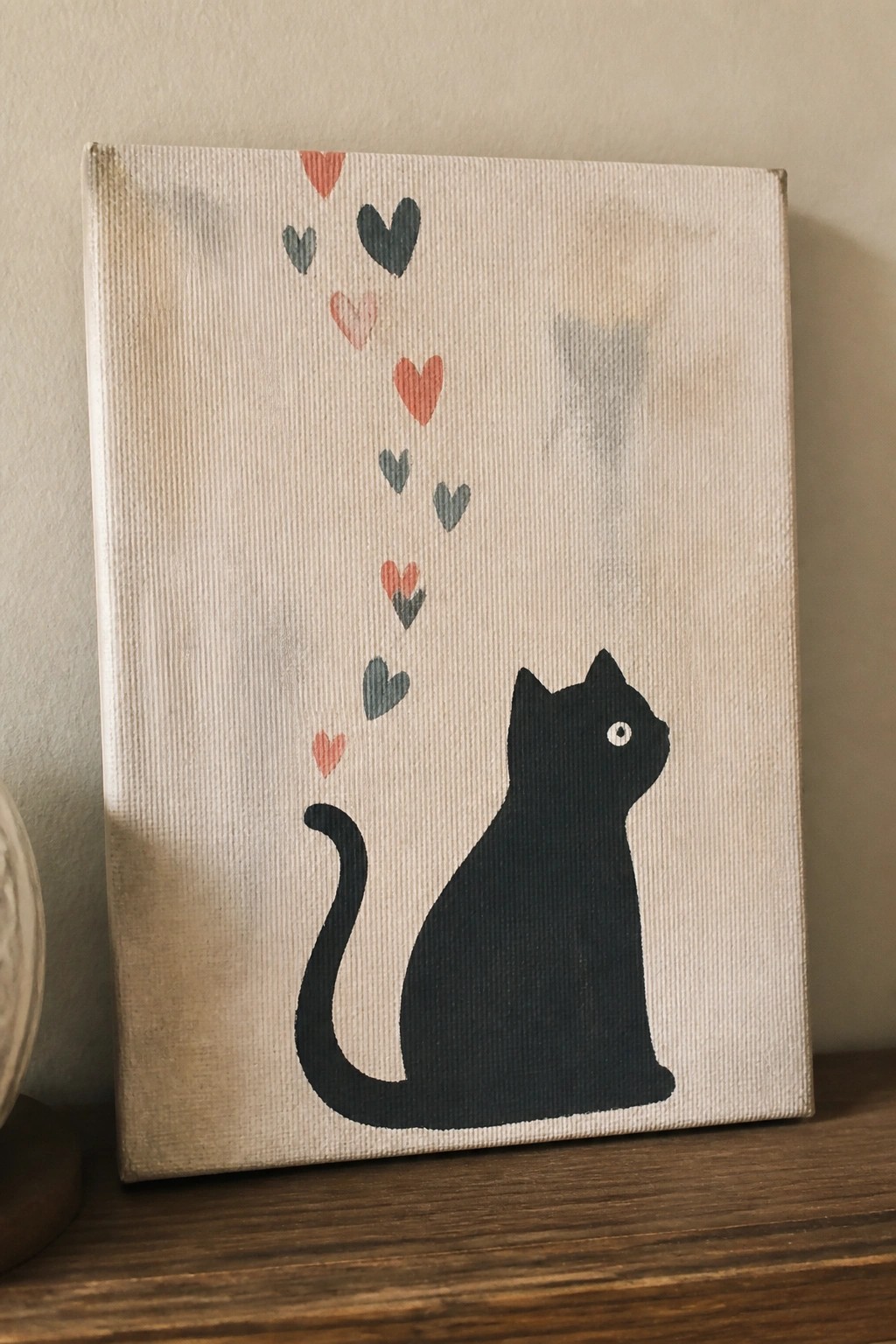 Black cat silhouette on canvas with colorful hearts floating above on wood ledge
