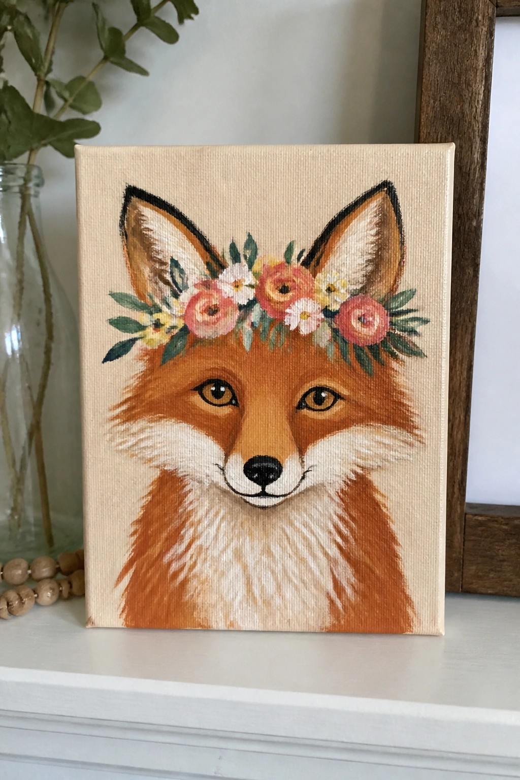 A canvas painting of a fox face wearing a crown of pink, orange, and yellow flowers against a plain light background.