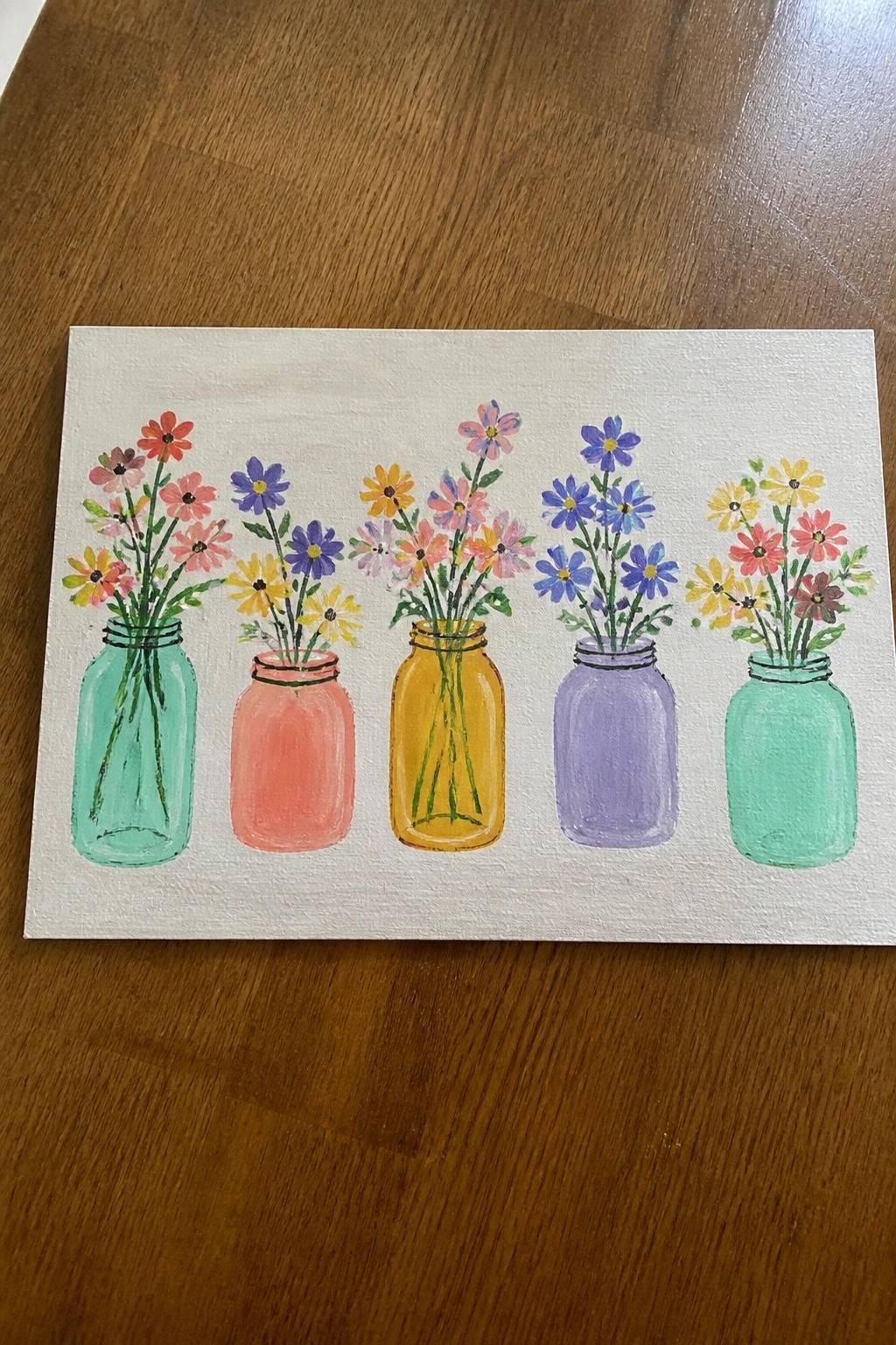 Five colorful mason jars with bright flowers on white canvas over wood
