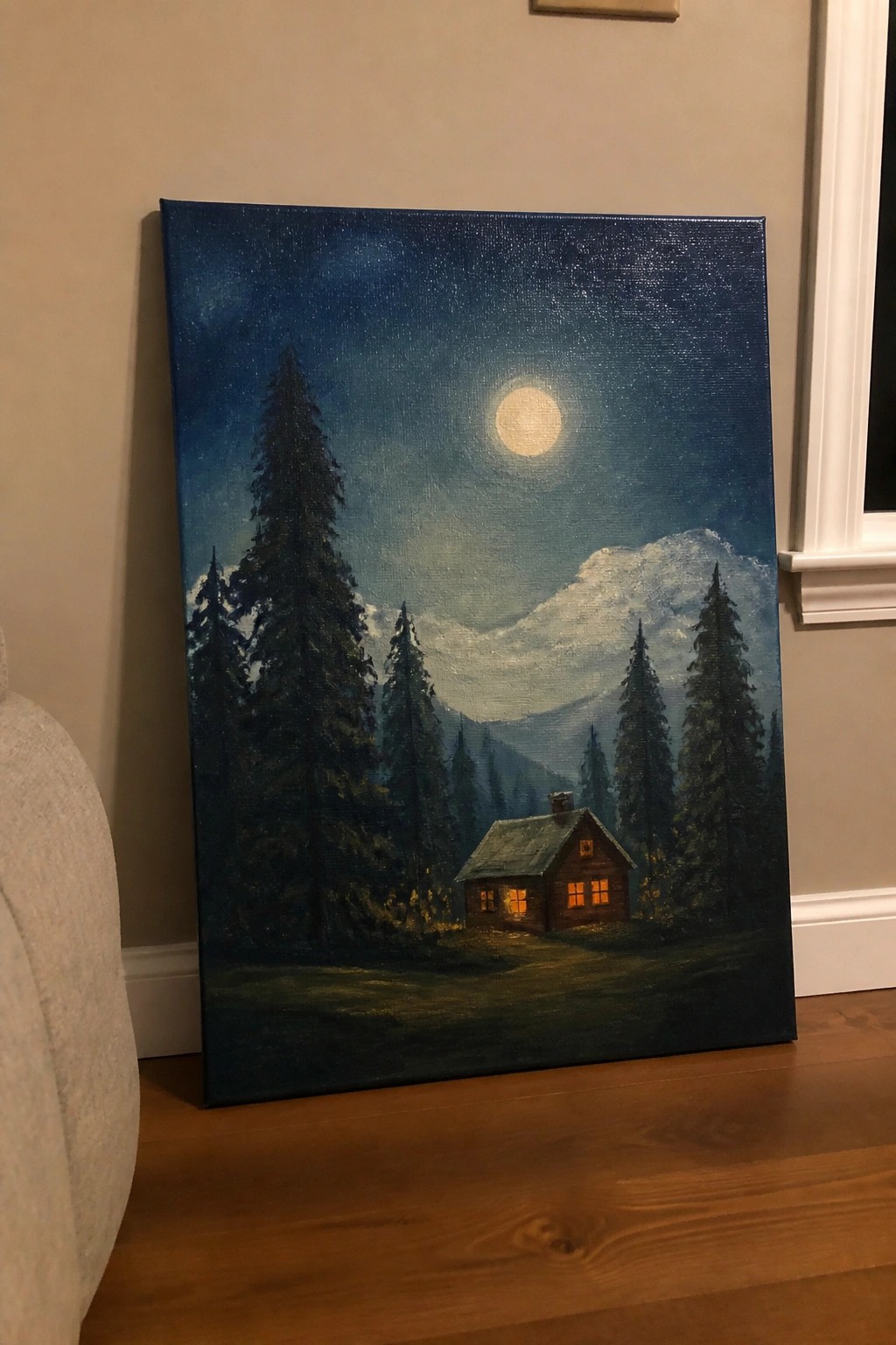 Moonlit cabin glowing in pine forest beneath full moon and snow-capped mountains