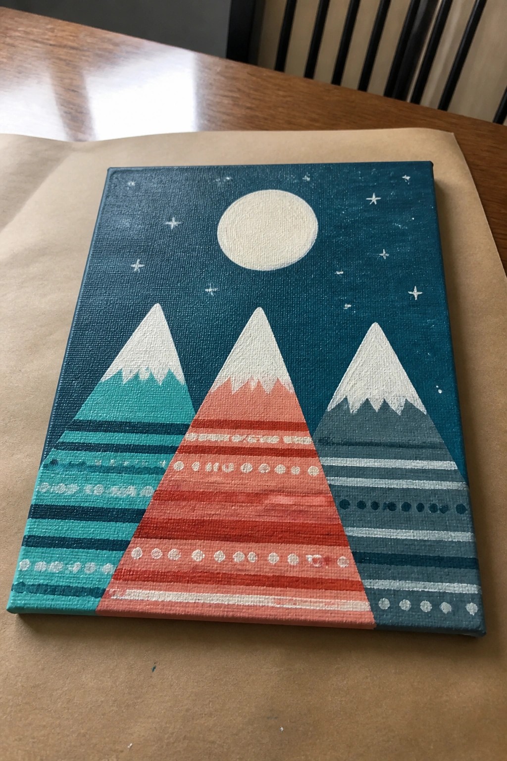 Colorful canvas painting of three patterned mountains under starry night sky with moon on table
