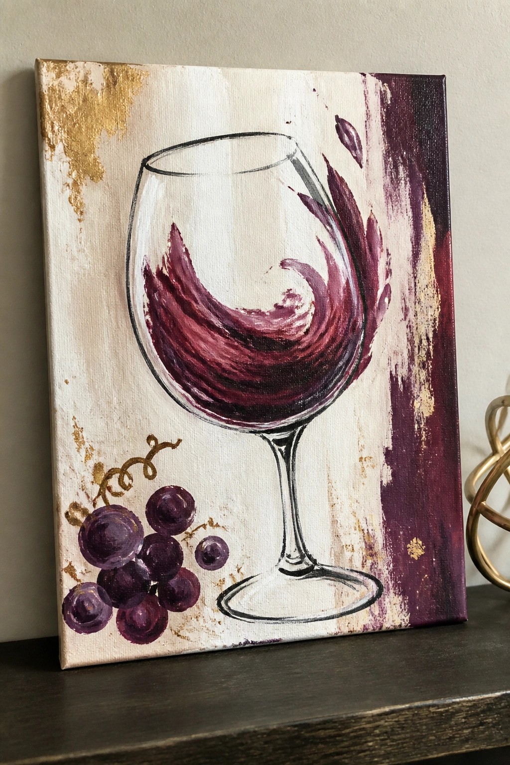 Abstract painting of swirling red wine in a glass with purple grapes and gold accents