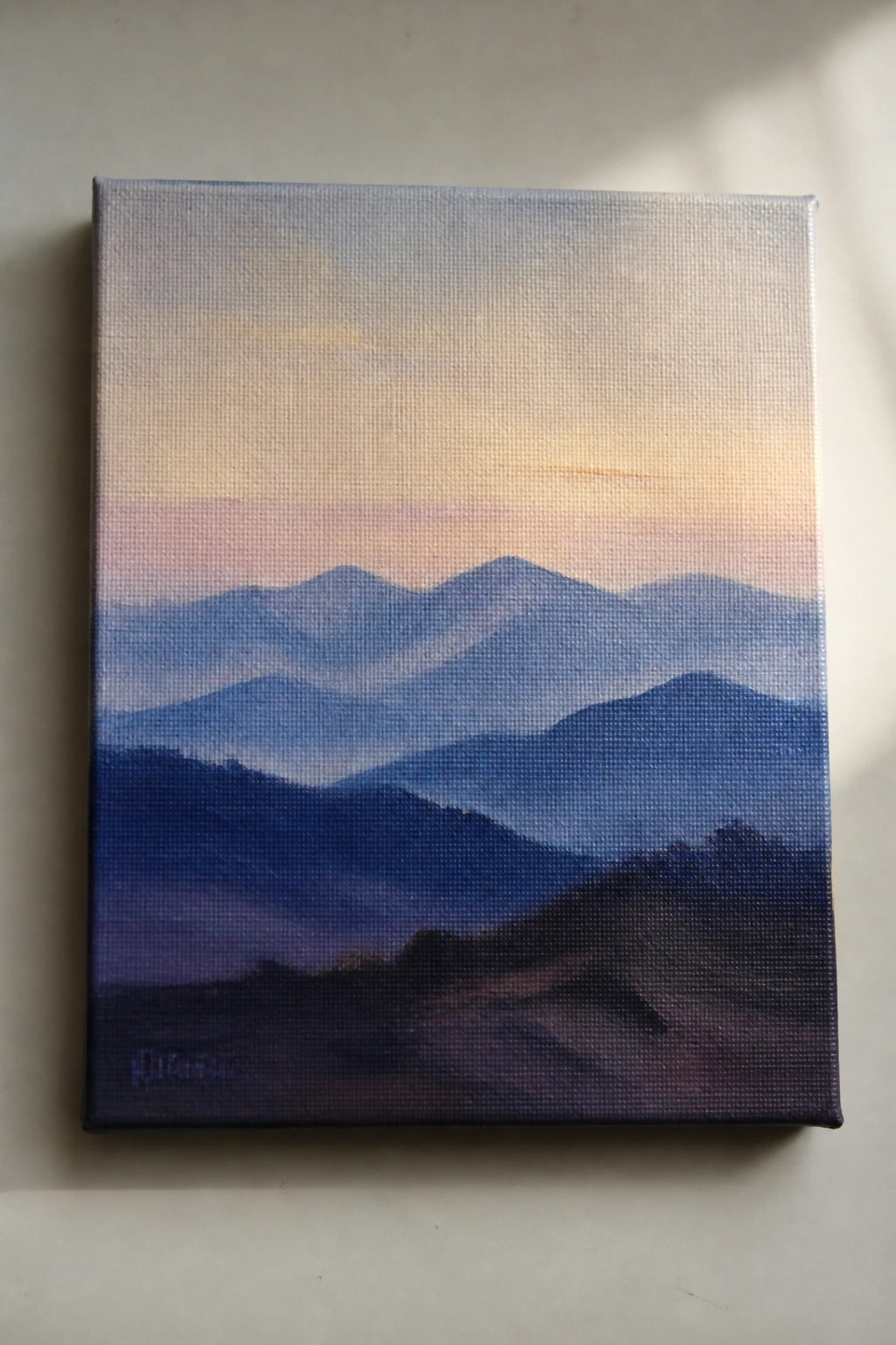 Layered blue mountains under a soft pink-orange sunset sky on canvas