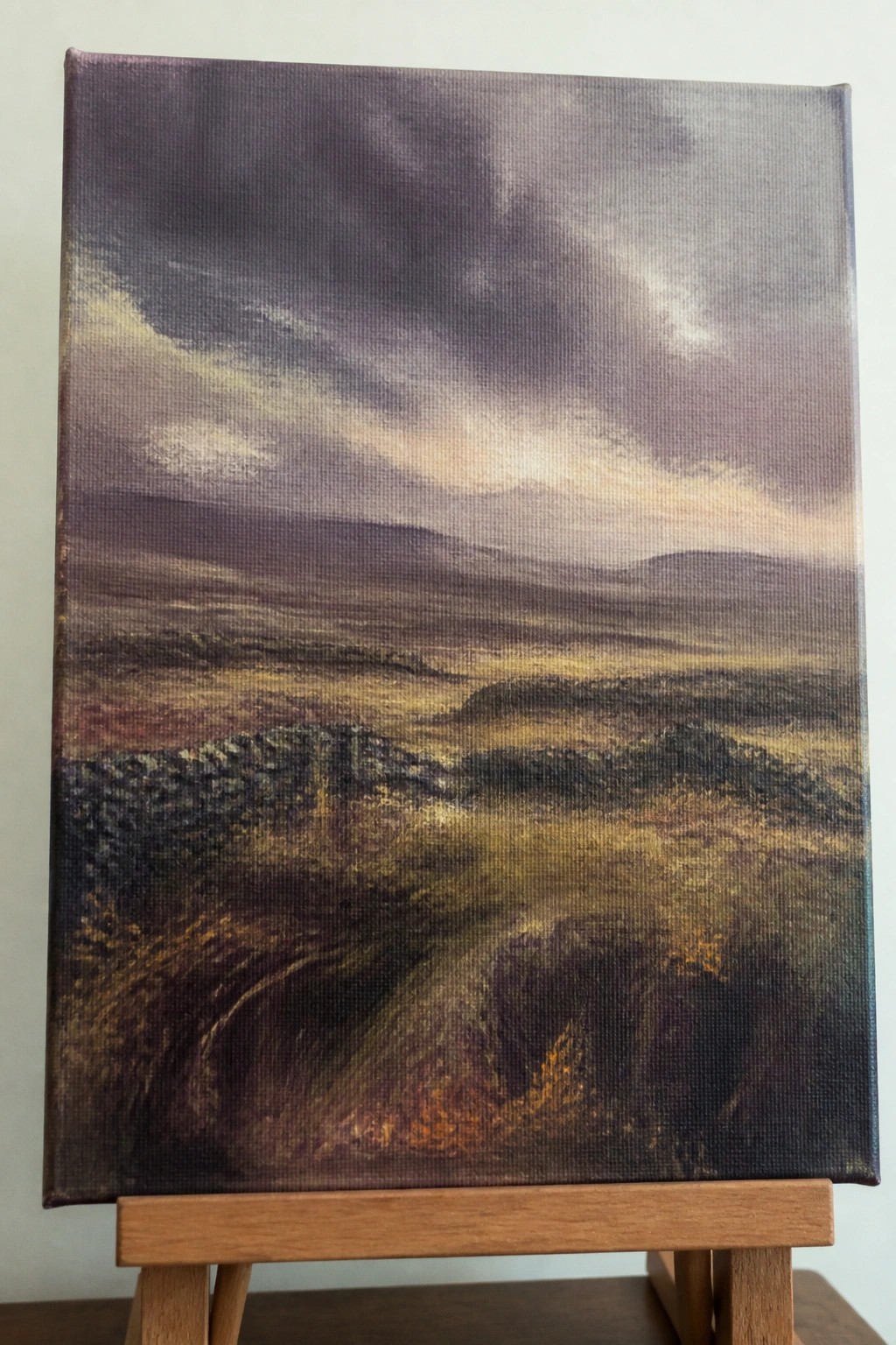 Dark moody landscape painting of hills under stormy skies on wooden easel.