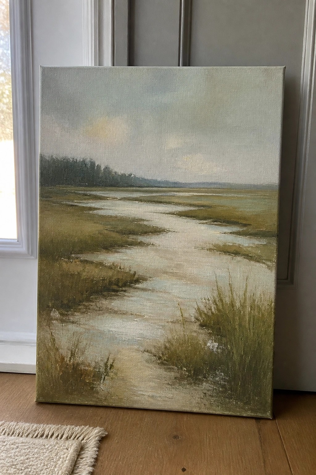 Large marsh landscape painting with winding water propped on wooden floor.