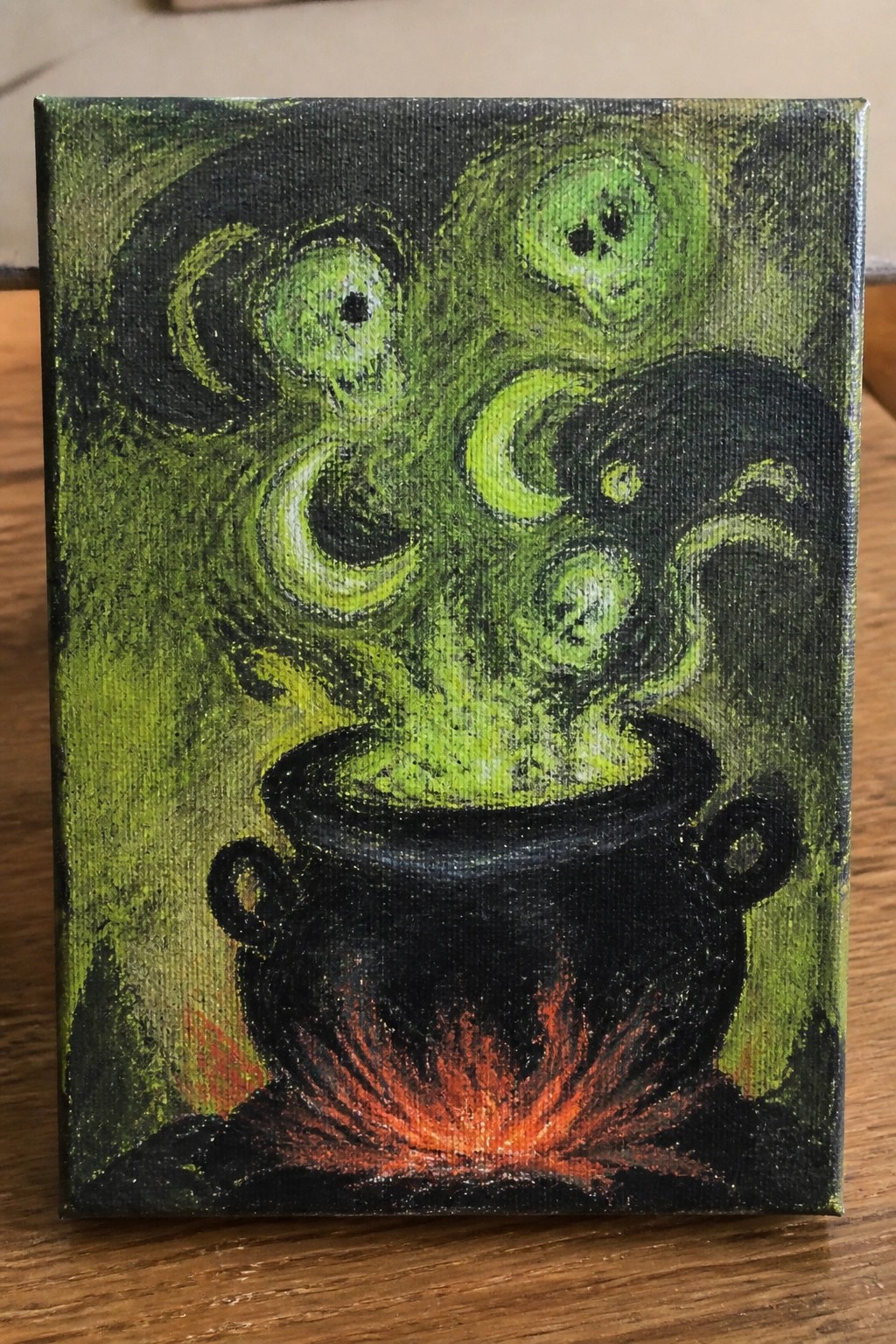 A painting of a black cauldron with green contents and flames underneath, with green skull-like shapes rising from it on a dark background.