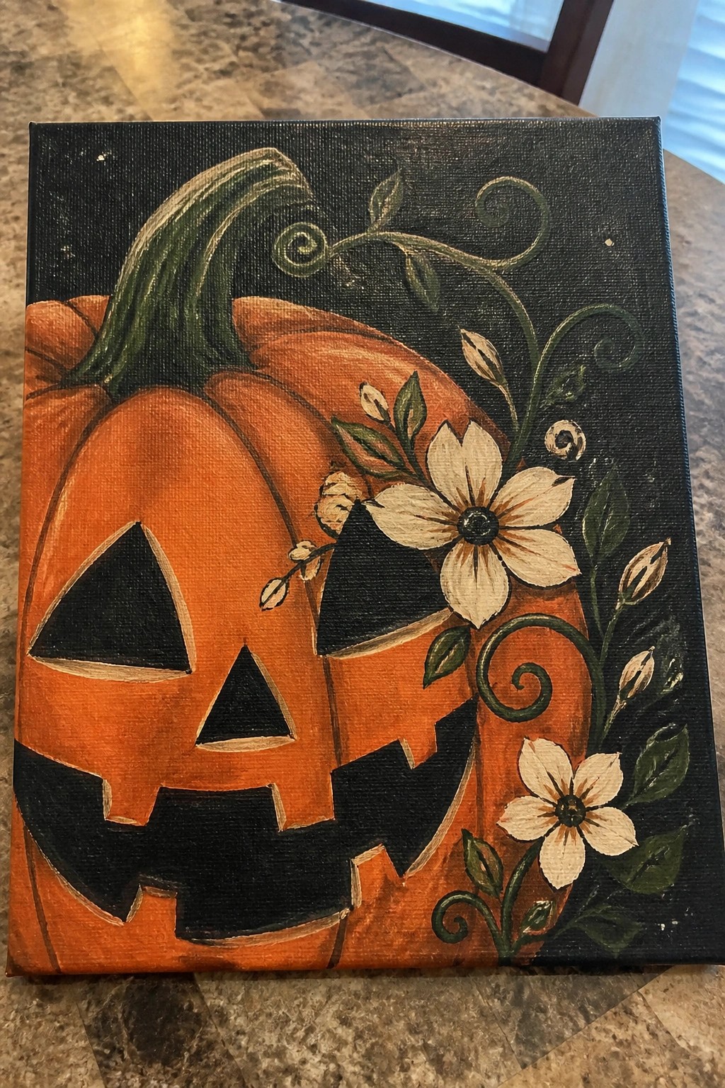 Orange jack-o'-lantern painting with white flowers and green vines on black canvas