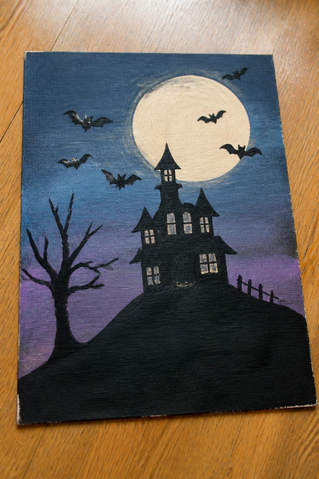 Silhouetted haunted house on hill under full moon with flying bats and bare tree