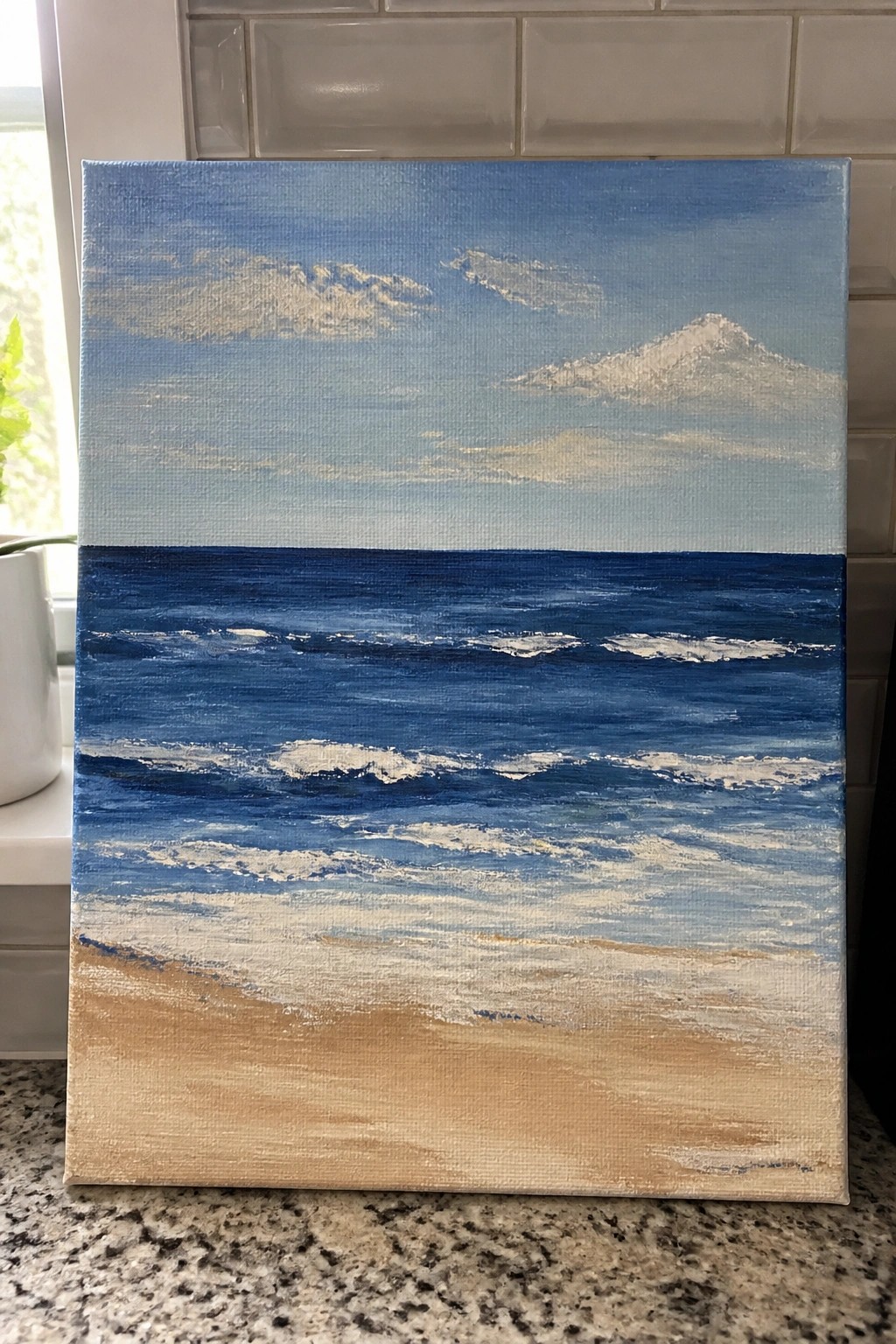 Seascape painting of blue ocean waves, sandy beach, cloudy sky, and mountain on canvas.