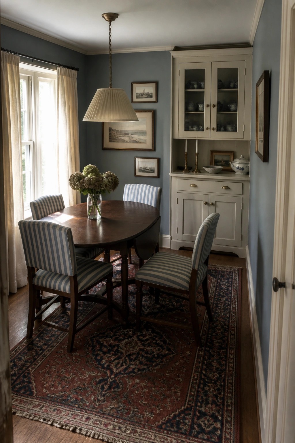 Round wooden dining table with striped chairs on red rug in blue room.
