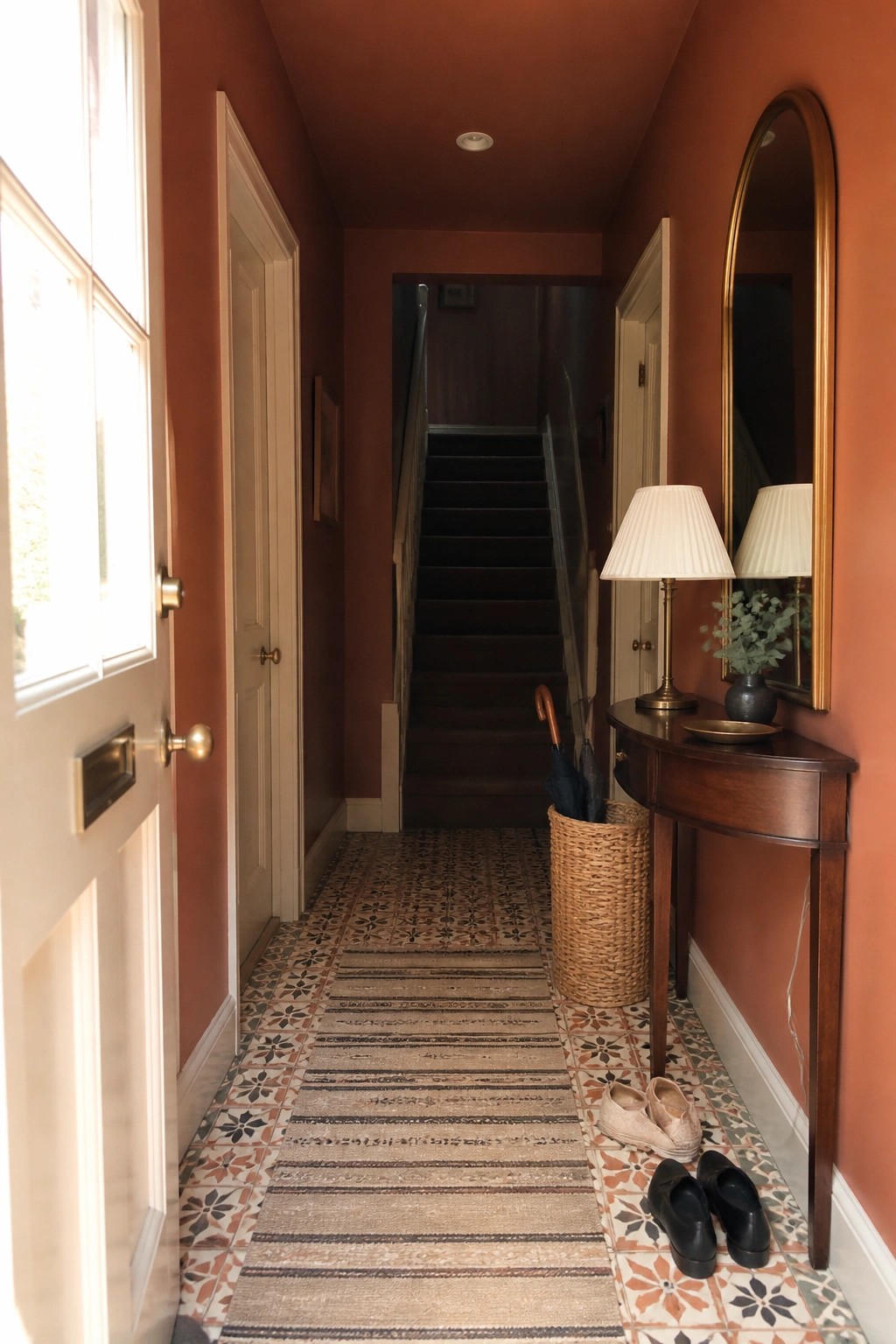 A narrow hallway painted warm terracotta with patterned tile flooring and a wooden console.