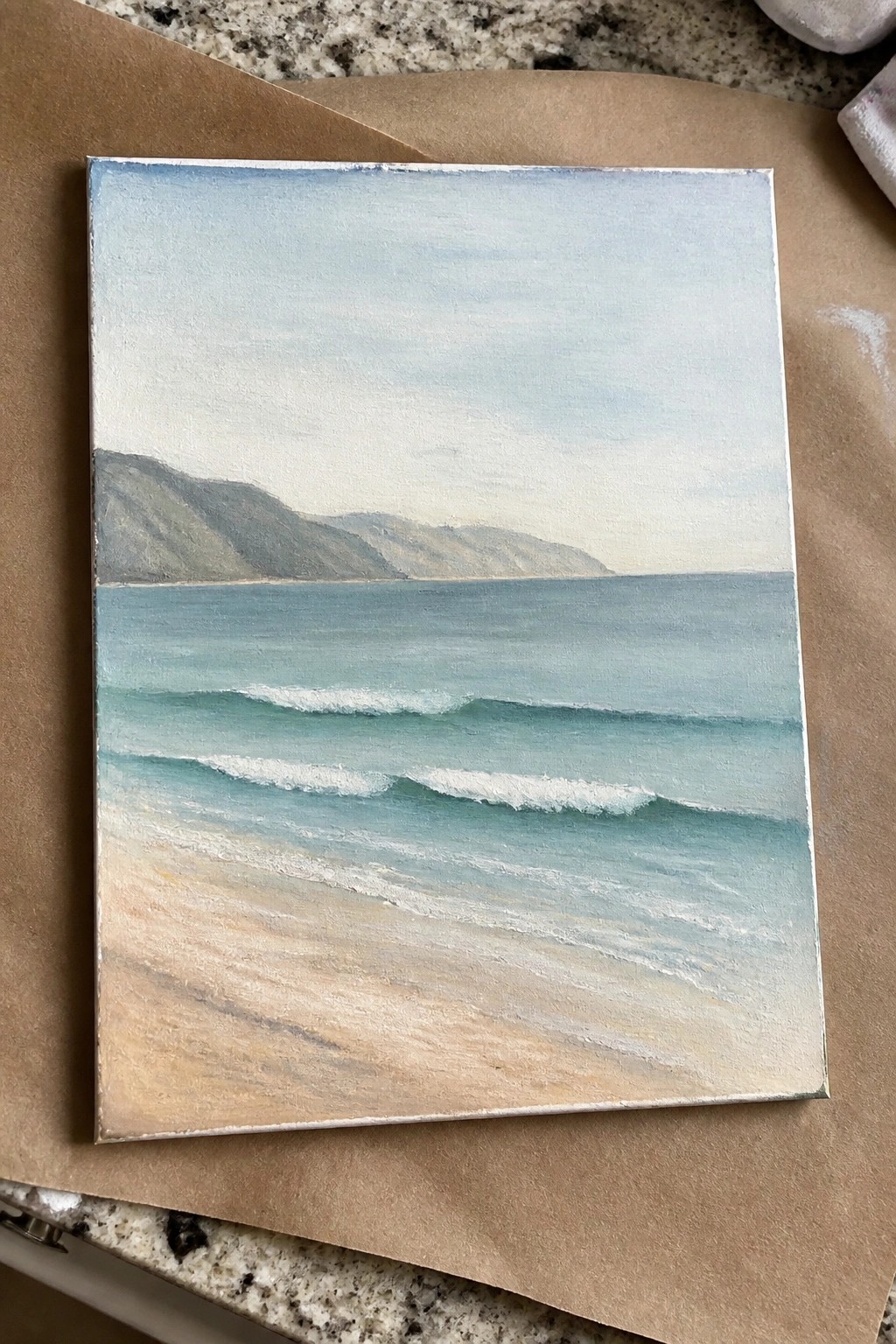 Seascape painting on canvas with turquoise waves, sandy beach, and distant mountains