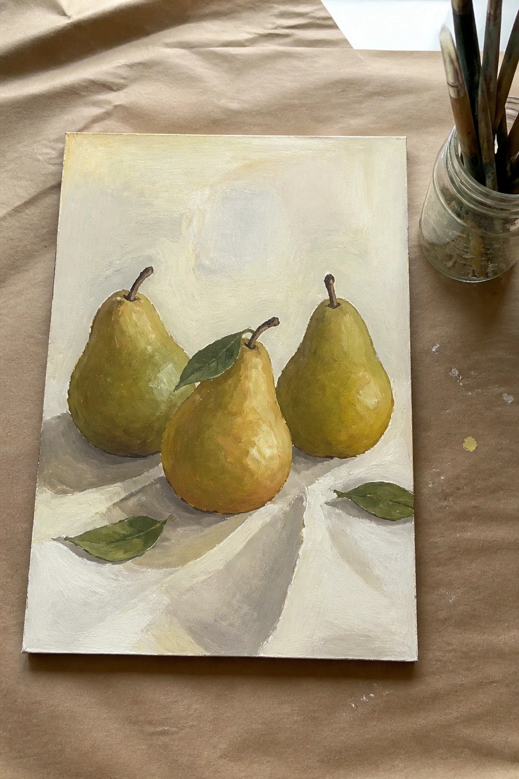 Realistic painting of three green pears on white cloth beside jar of brushes