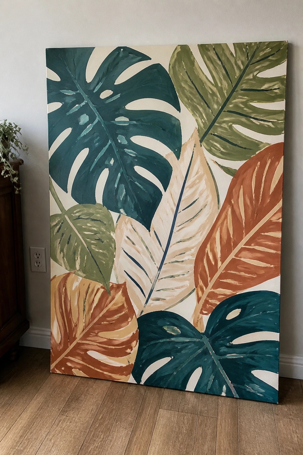 Large canvas painting of colorful tropical leaves leaning against white wall on wooden floor