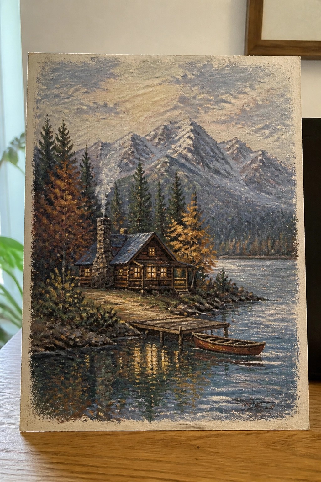 Autumn landscape painting of a log cabin by a mountain lake with dock and boat.