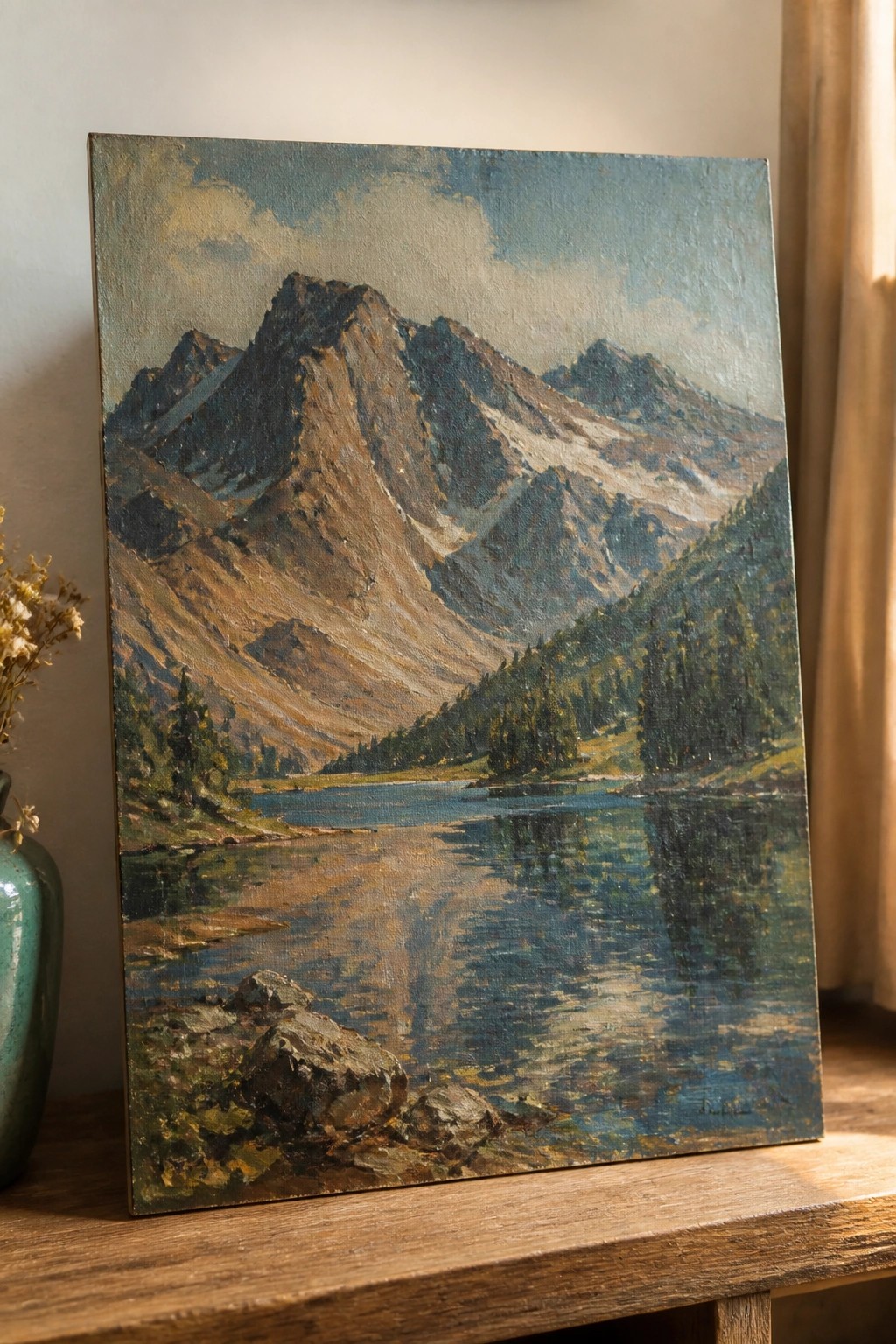 Oil painting of rugged mountains reflected in calm blue lake on wooden table.