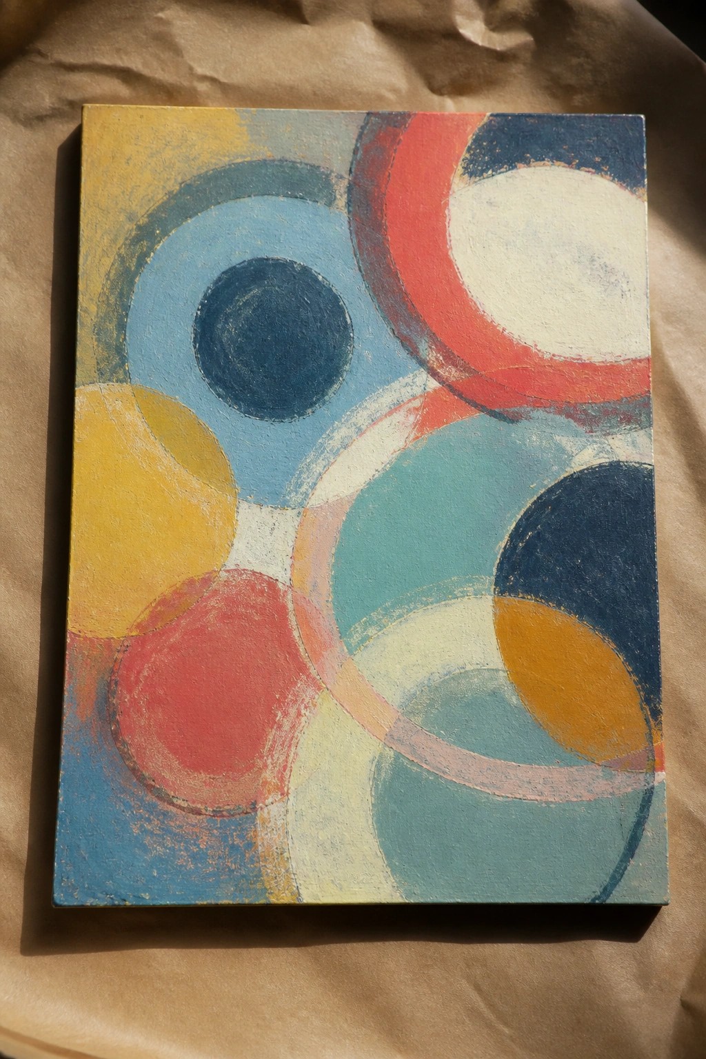 An abstract oil painting on canvas showing overlapping circles and rings in yellow, blue, red, teal, navy, and white.