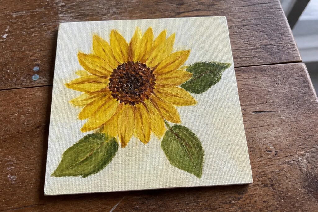 Yellow sunflower with brown center and green leaves on beige canvas