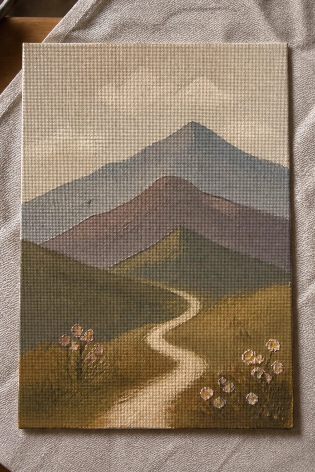 Canvas painting of winding path through hills to layered mountains with foreground flowers.