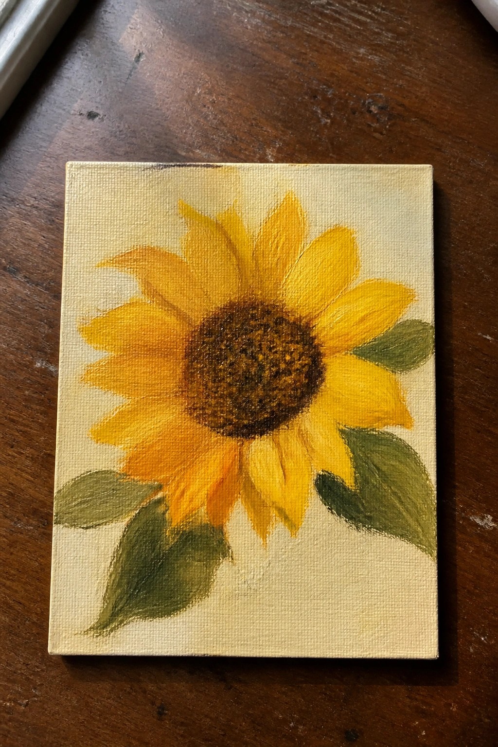 Yellow sunflower with brown center and green leaves on beige canvas