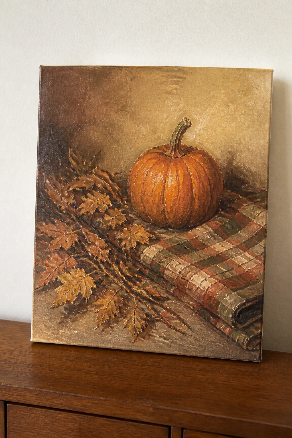 Still life painting of orange pumpkin on plaid cloth with autumn leaves