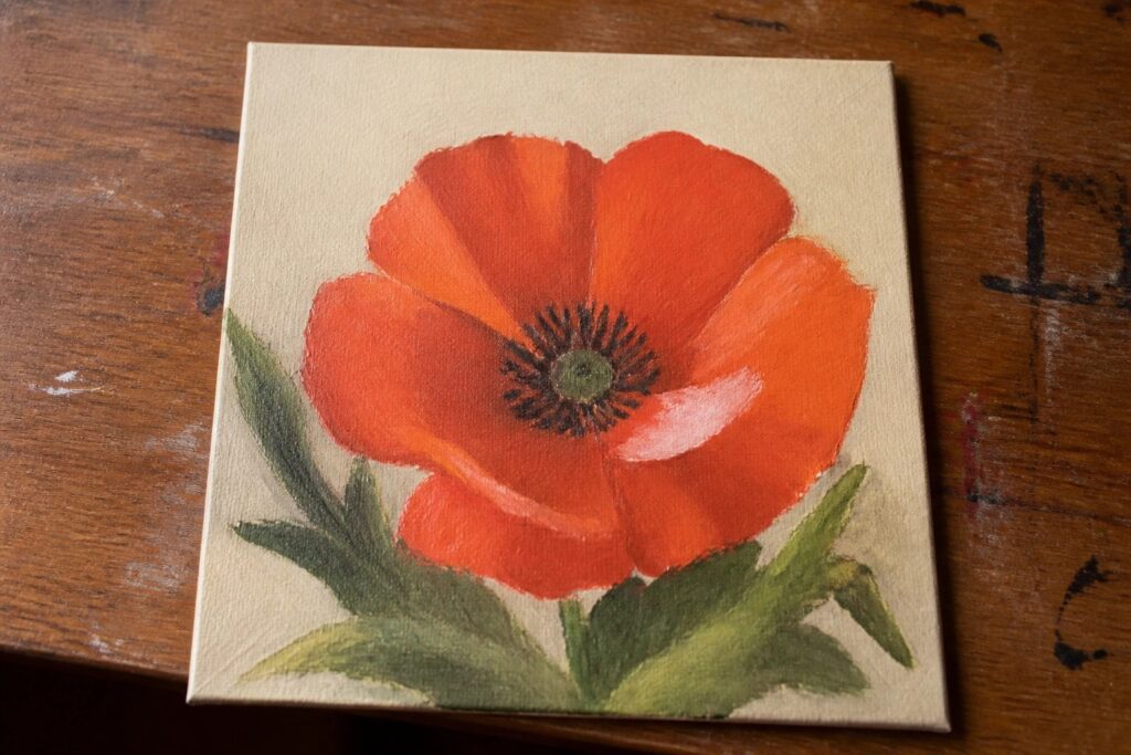 Vibrant red poppy with dark center and green leaves on beige canvas.