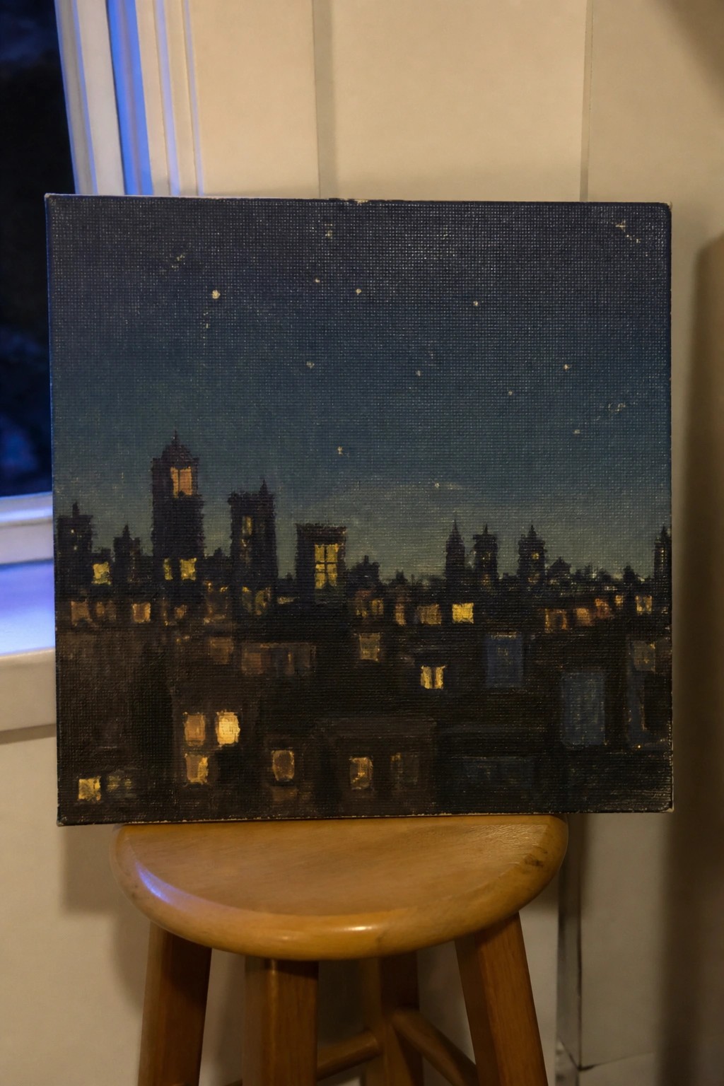 Painting of nighttime cityscape with glowing windows on wooden stool