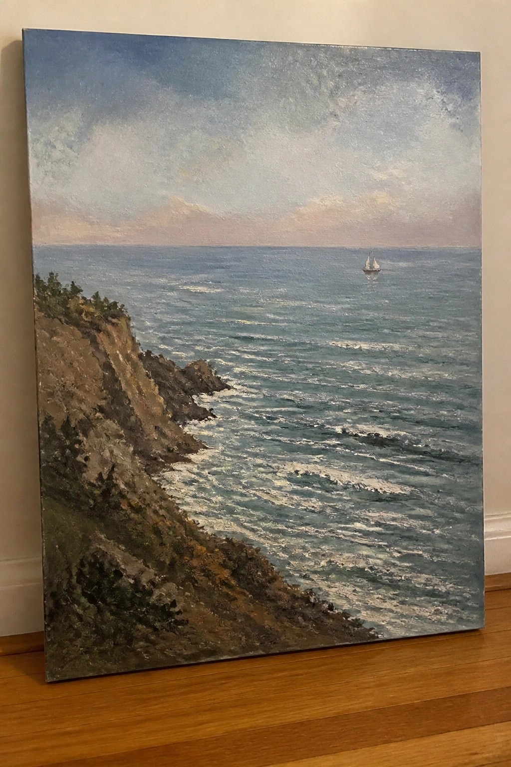 Seascape oil painting of rocky cliff, crashing waves, and distant sailboat under pink-blue sky