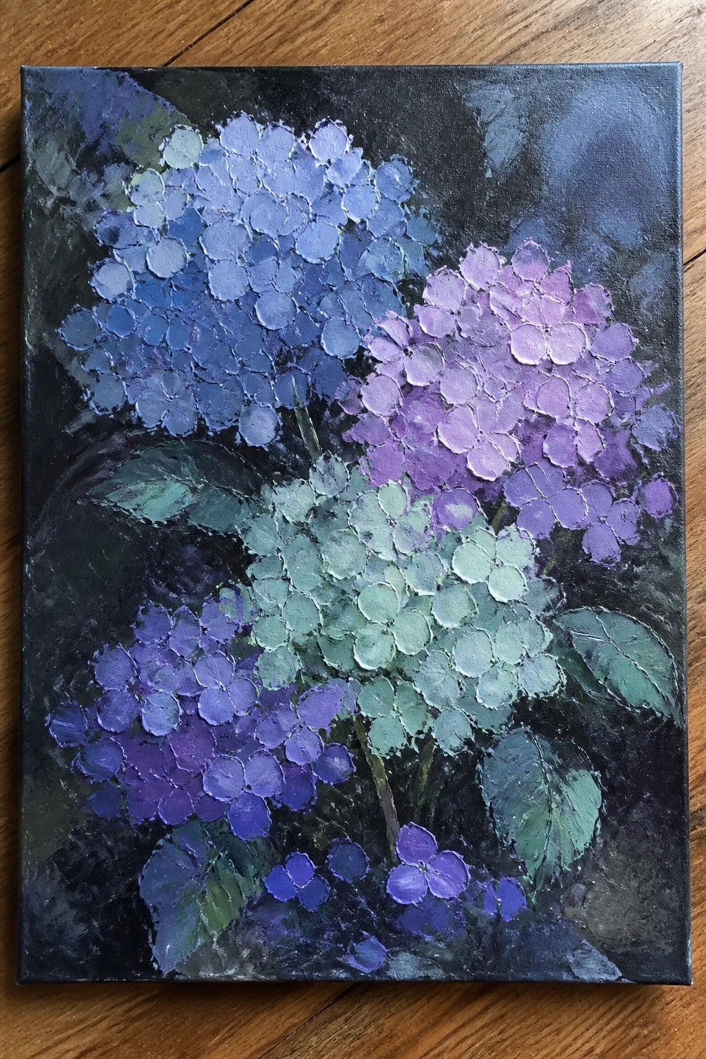 A painting of several hydrangea flower clusters in shades of blue, purple, and green with thick textured paint on a dark background.