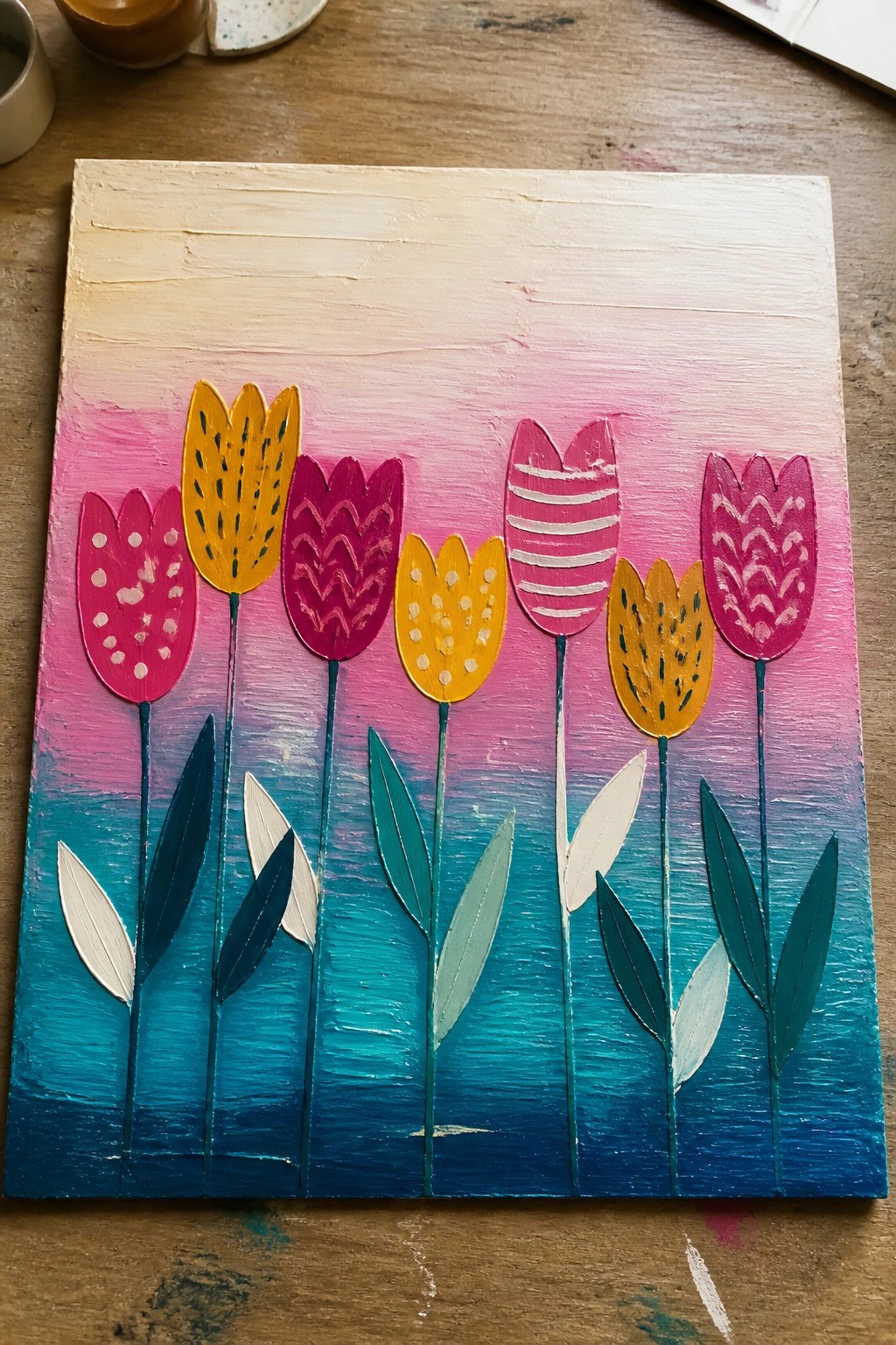 A painted canvas shows eight colorful tulips with patterned petals lined up on a pink-to-blue gradient background with simple leaves at the base.