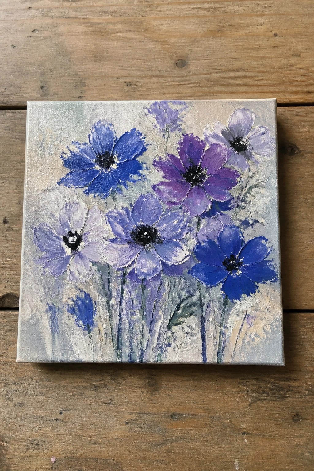 Square canvas with blue and purple flowers on wooden surface
