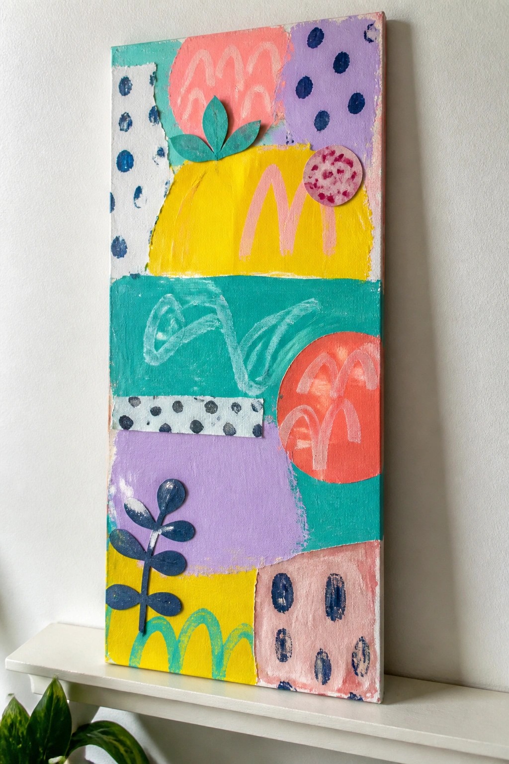 Colorful abstract painting with geometric shapes, patterns, dots, and leaf cutouts on canvas.