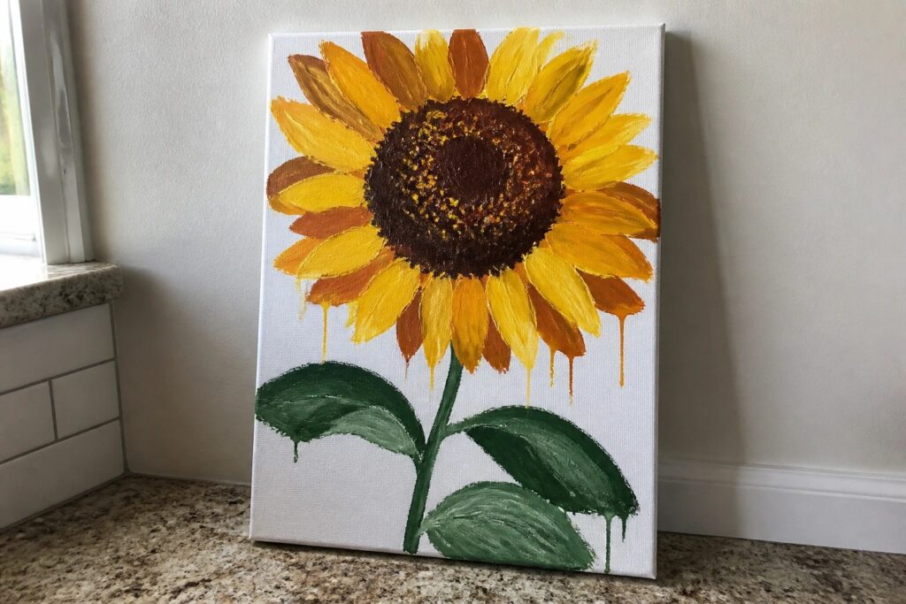 Yellow sunflower painting with brown center, green leaves, and yellow drips on canvas