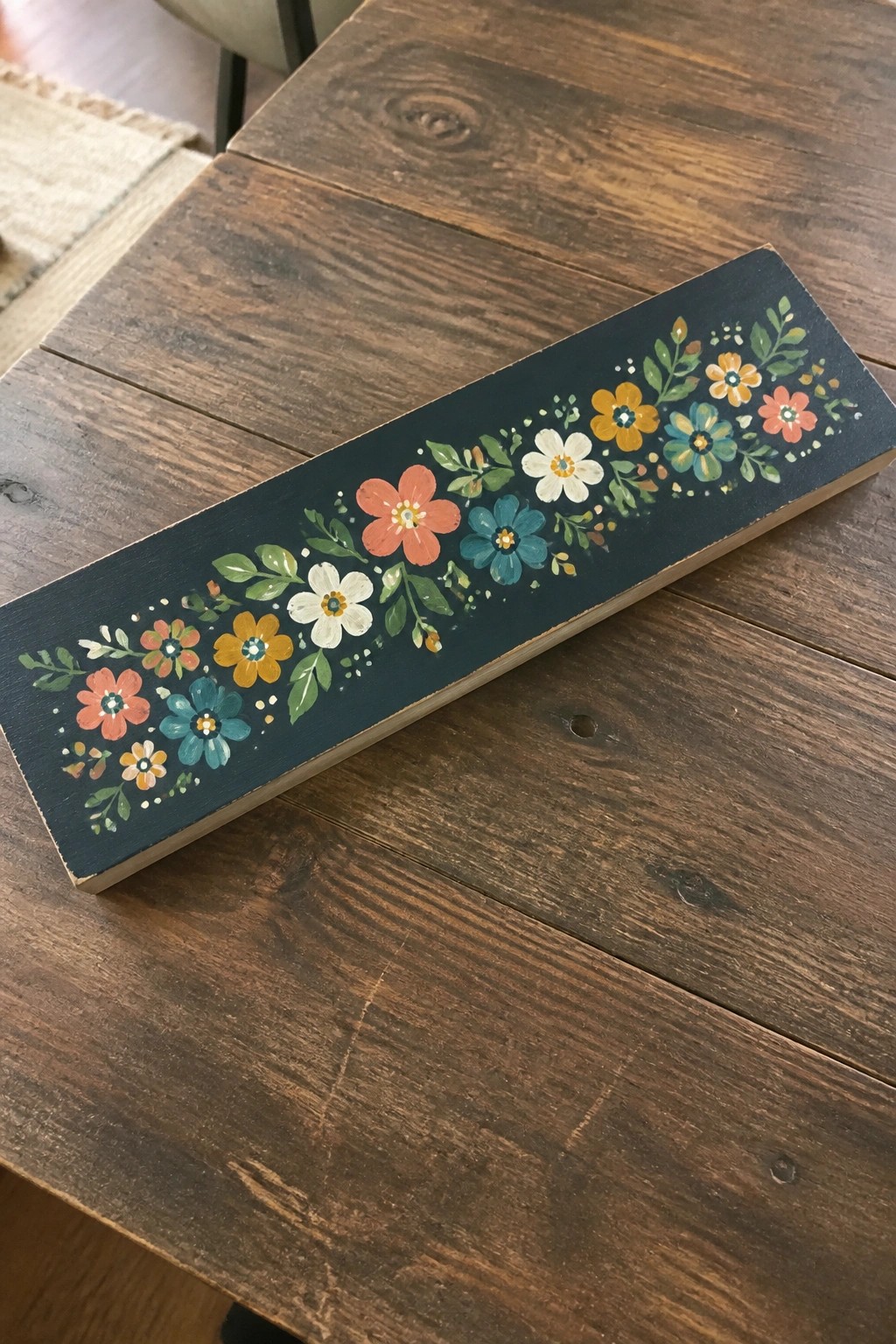 Hand-painted colorful flowers adorn a long dark teal wooden plank on a table.